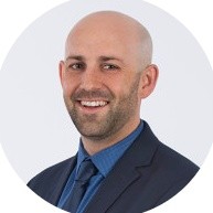 Smiling bald man in a suit and tie against a white background.